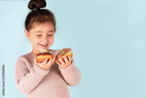 Little happy cute girl eating donuts on blue background. Child having fun with donut.