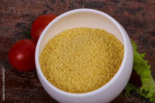 Raw couscous in the bowl served salad leaves, tomato and pepper