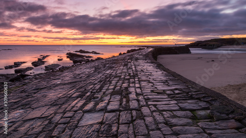 The stone pier at the harbour mouth of Cullercoats Bay on the coast of North Tyneside, England, UK. At sunrise with a colourful sky, taken at low tide.