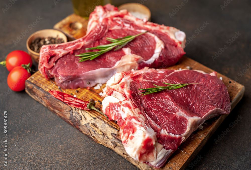 raw beef steaks with spices and rosemary on a stone background