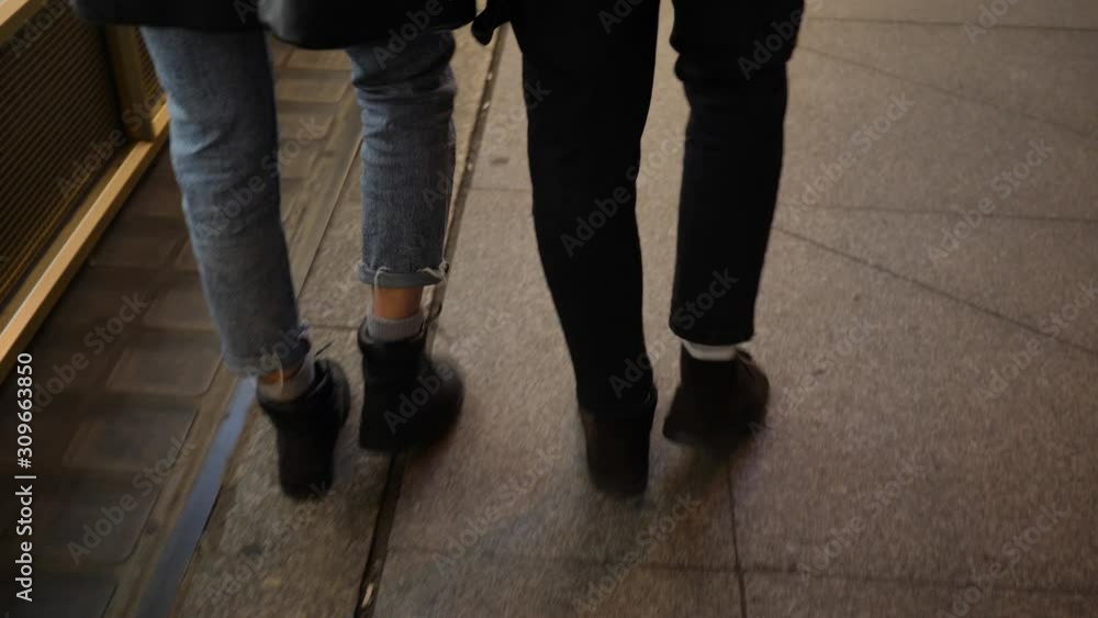 Young people couple legs camera walking night city sidewalk having date and relationships Young people couple legs camera walking night city sidewalk having date and relationships