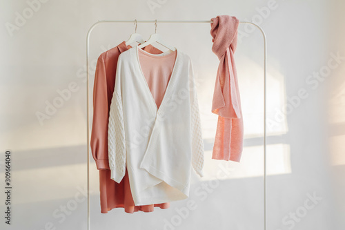 Female clothes in pastel pink  color on hanger on white background.  Elegant dress   jumper  shirt and scarf. Spring cleaning home wardrobe. Minimal concept.