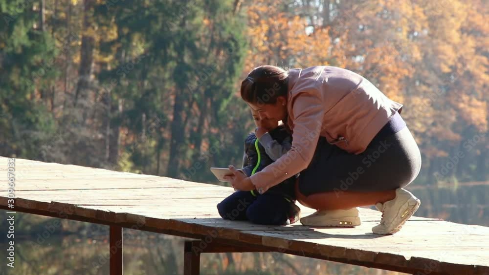 Kid and his mom using smartphone in the autumn park Kid and his mom using smartphone in the autumn park