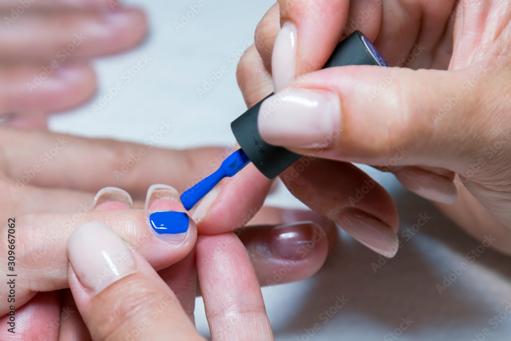 Beautiful manicure process. Nail polish being applied to hand, polish is a blue color. close up Beautiful manicure process. Nail polish being applied to hand, polish is a blue color. close up