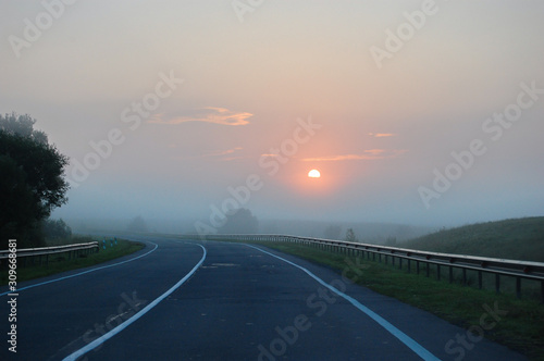 Empty asphalt road in the light of the rising sun and morning fog