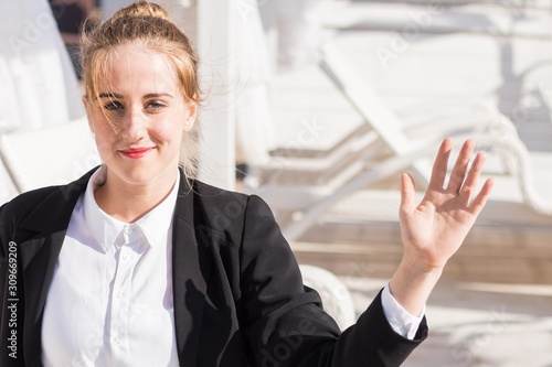 attractive Caucasian blond business woman in black jacket waving her hand in greeting while office meeting 