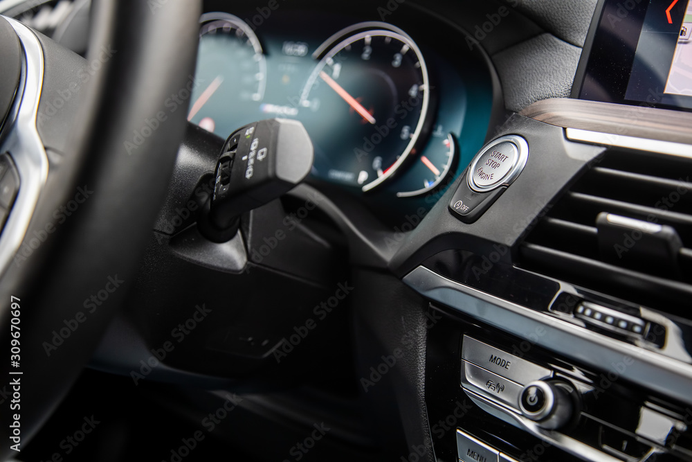 close-up start-stop button under the steering wheel of a modern car. speedometer in blur on the background