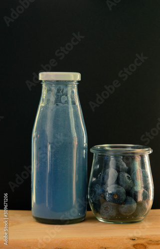 blue matcha and blueberry smoothie drink and blueberries in glass jar on dark black background