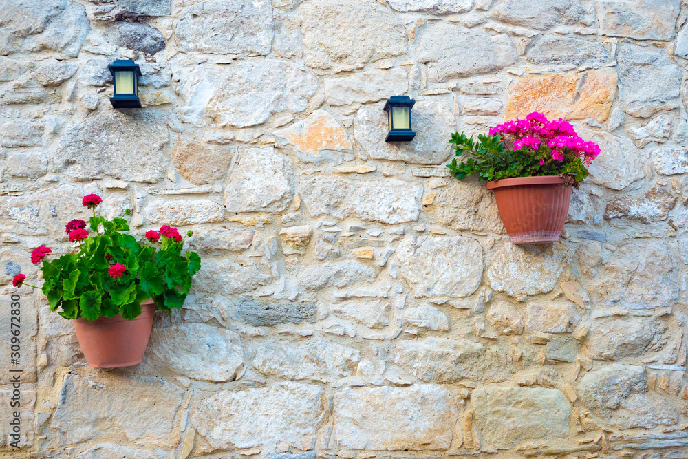 Cyprus. Kuklia. The wall of the building is made of shell. The wall is decorated with flowers and lanterns. Pelargonium in pots. Background of yellow stones. Decoration of the facade of the house.