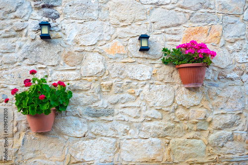 Cyprus. Kuklia. The wall of the building is made of shell. The wall is decorated with flowers and lanterns. Pelargonium in pots. Background of yellow stones. Decoration of the facade of the house. © Grispb
