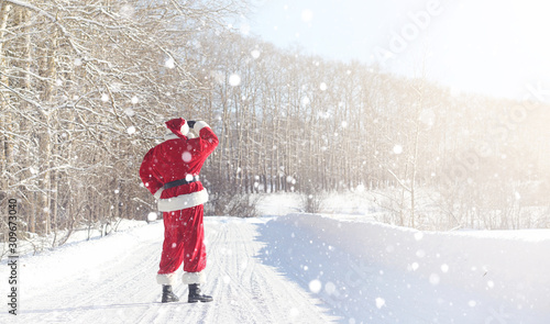 Santa Claus comes with gifts from the outdoor. Santa in a red suit with a beard and wearing glasses is walking along the road to Christmas. Father Christmas brings gifts to children.