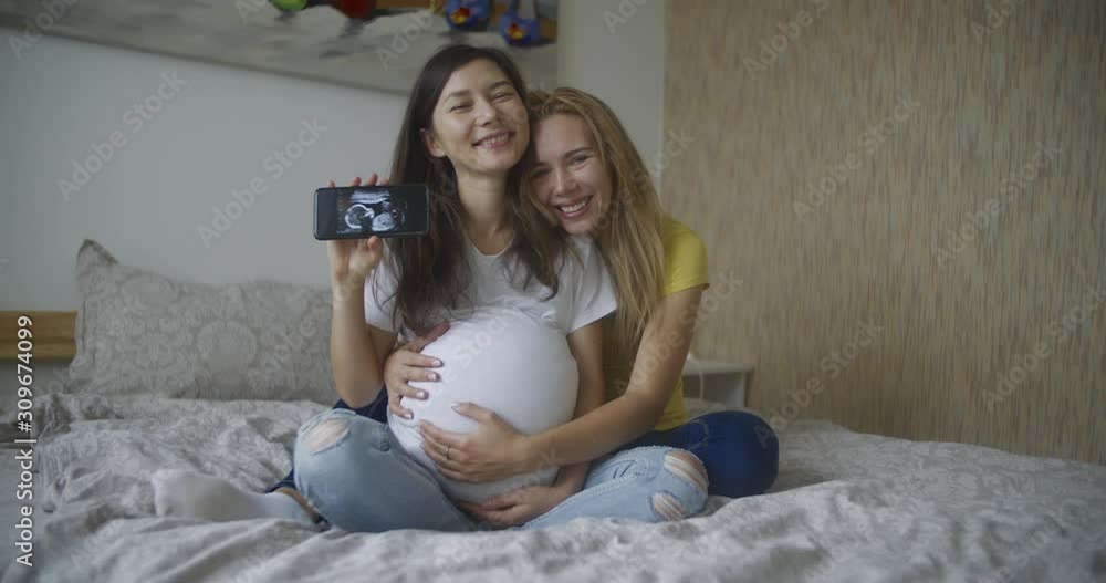 Pregnant multinational lesbian couple shows at an ultrasound image of his baby on the phone. LGBT Pregnant multinational lesbian couple shows at an ultrasound image of his baby on the phone. LGBT
