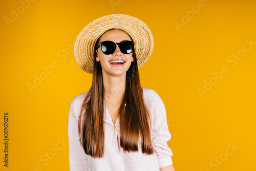 a girl on vacation, wearing a straw hat and black glasses, laughing joyfully. background yellow