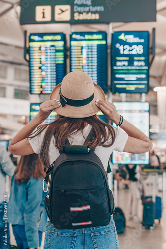 the tourist at the airport looks at the scoreboard, standing with his back to the camera, a backpack behind his shoulders, a hat on his head