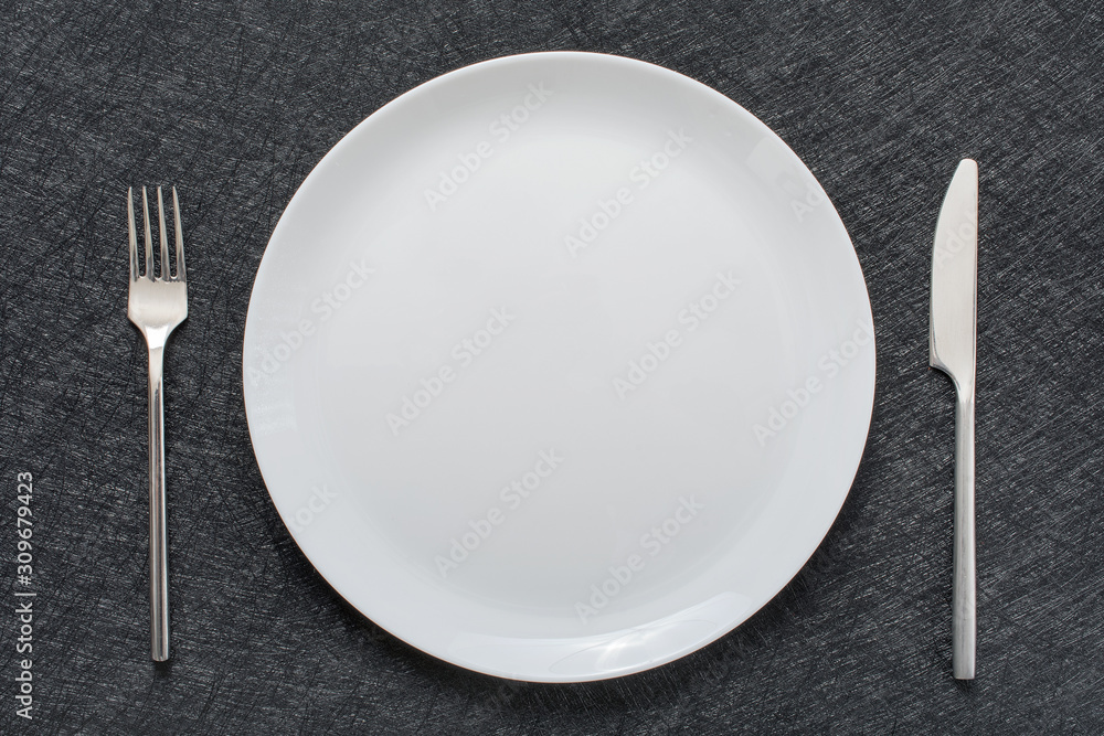 White empty plate with fork and knife on a grey tablecloth, top view. White empty plate with fork and knife on a grey tablecloth, top view.