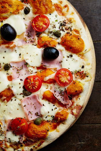 Tasty pizza with ham, cherry tomatoes, mozzarella cheese, black olives and capers on wooden background. Top view. 