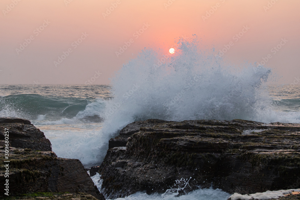 Fototapeta premium A wave crash into the rocks with sun on the background.