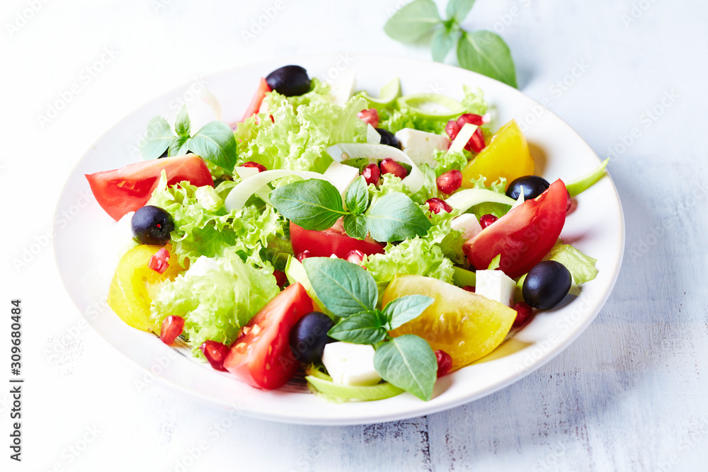  Healthy salad with pomegranate seeds, tomatoes, black olives, lettuce and fresh herbs. Bright background. Close up.