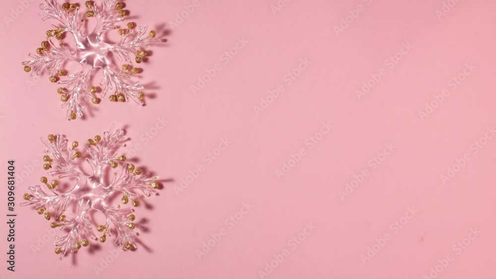 Flat lay, top view, stop motion animation. Two transparent snowflakes with golden glitters at the tips spin around its axis on a bright pink background on the left side. Christmas concept Flat lay, top view, stop motion animation. Two transparent snowflakes with golden glitters at the tips spin around its axis on a bright pink background on the left side. Christmas concept