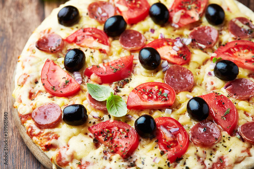 Pizza with sausage, tomatoes, black olives and herbs. Home made food. Concept for a tasty and hearty meal. Close up. 