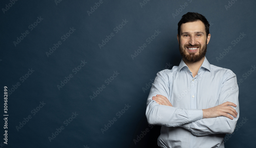 Happy young man. Portrait of handsome young bearded man keeping arms crossed and smiling.