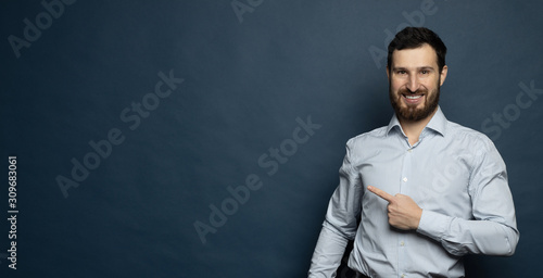 Portrait of cheerful satisfied handsome attractive fashionable bearded man dressed in formal outfit pointing on empty blank copyspace isolated on blue background