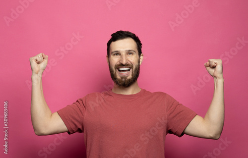 Young bearded man celebrating victory over pink background.