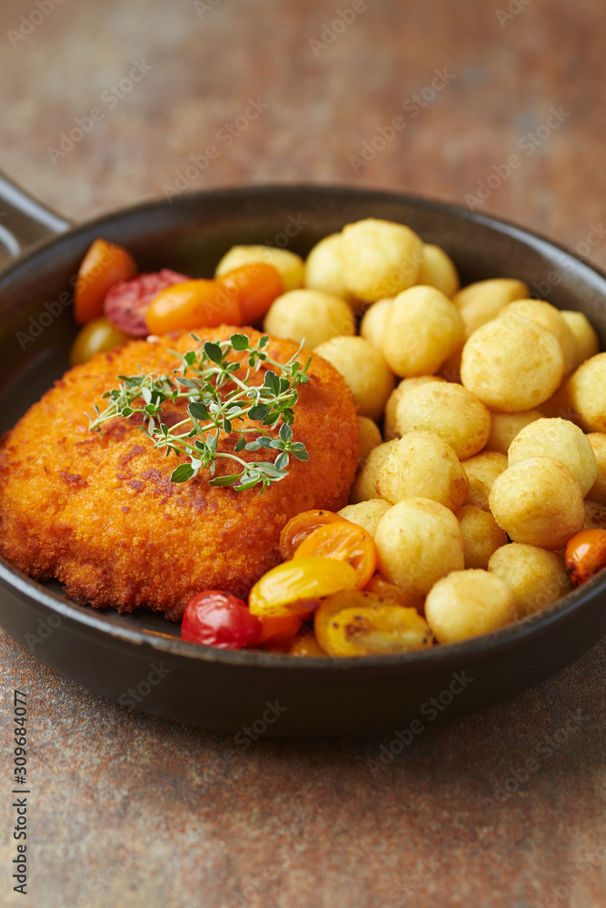 Breaded Chicken Breast with fried potatoes and fresh herbs. Rustic background. 