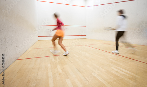 Two female squash players in action on a squash court (motion blurred image; color toned image)