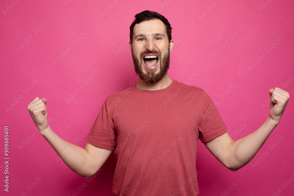 Young bearded man celebrating victory over pink background. Young bearded man celebrating victory over pink background.