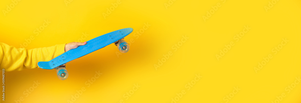 hand holding blue skate board over yellow background, panoramic mock up image hand holding blue skate board over yellow background, panoramic mock up image
