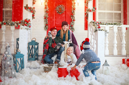 Joyful family with children playing snowballs in courtyard of snowy house in winter on Christmas