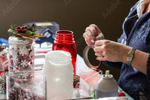 Middle age woman making Christmas crafts with snow painted jars, holly and poinsettias. 