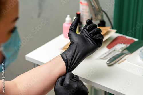 Nurse or cosmetologist woman putting on medical latex black gloves  closeup.