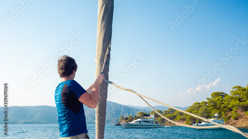 man in blue t-shirt stands on the deck near the sail, sailing and yachting, concept.