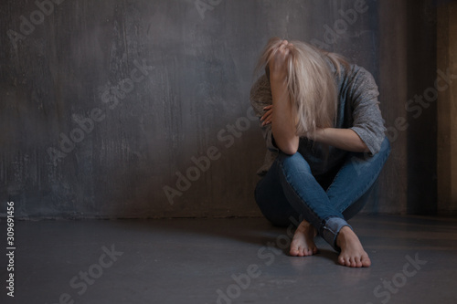 Sad woman sits on the floor. Depression and chronic fatigue. Young beautiful blonde in a gray sweater and jeans