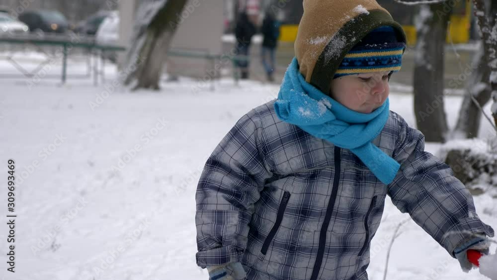 Young Beautiful Mother And Cute Child Play Outdoors During Snowfall. Winter City Young Beautiful Mother And Cute Child Play Outdoors During Snowfall. Winter City