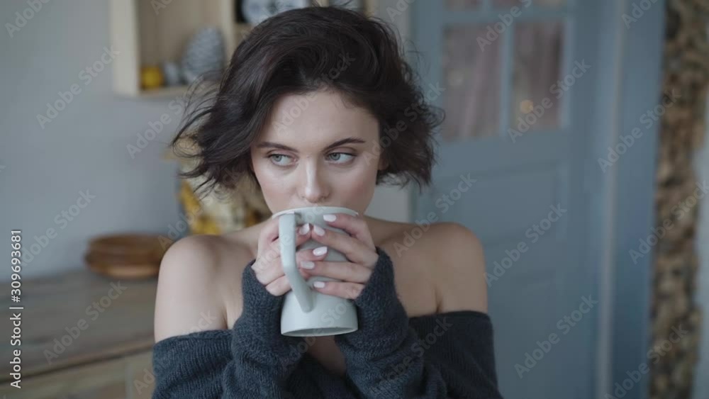Cute woman in cozy sweater thoughtfully drinks tea in room Cute woman in cozy sweater thoughtfully drinks tea in room