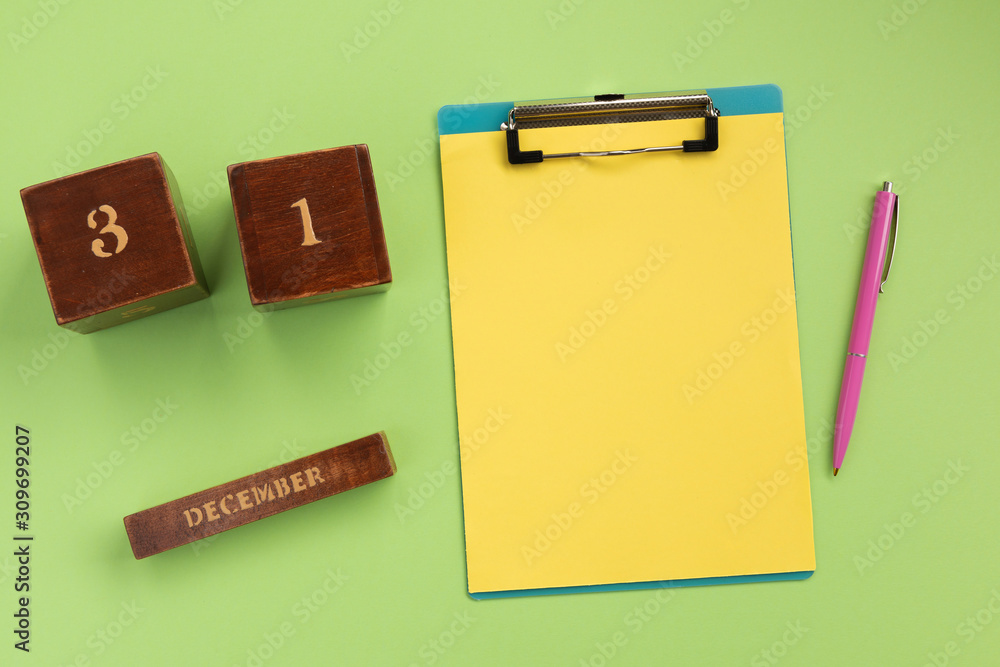 Christmas or New Year planning concept. Clipboard, wooden calendar, pen, on green background. Flat lay, top view, copy space. Christmas or New Year planning concept. Clipboard, wooden calendar, pen, on green background. Flat lay, top view, copy space.
