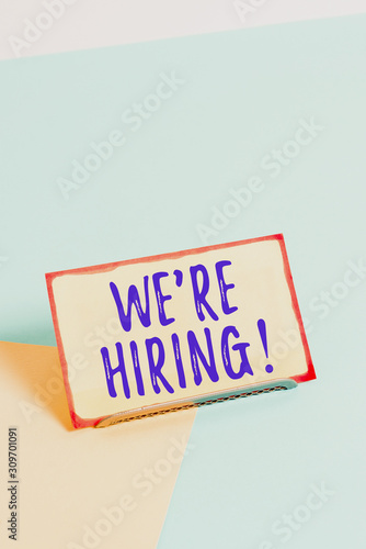 Text sign showing We Re Hiring. Business photo showcasing recently employ someone or pay someone to do particular job Paper placed tilted above buffer wire on soft pastel multi colours backdrop