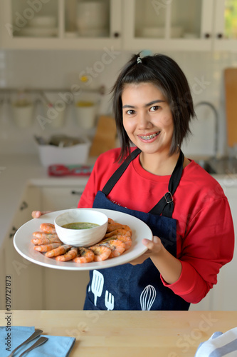 Asian women carrying dishes of Baked salted shrimp and spicy seafood sauce