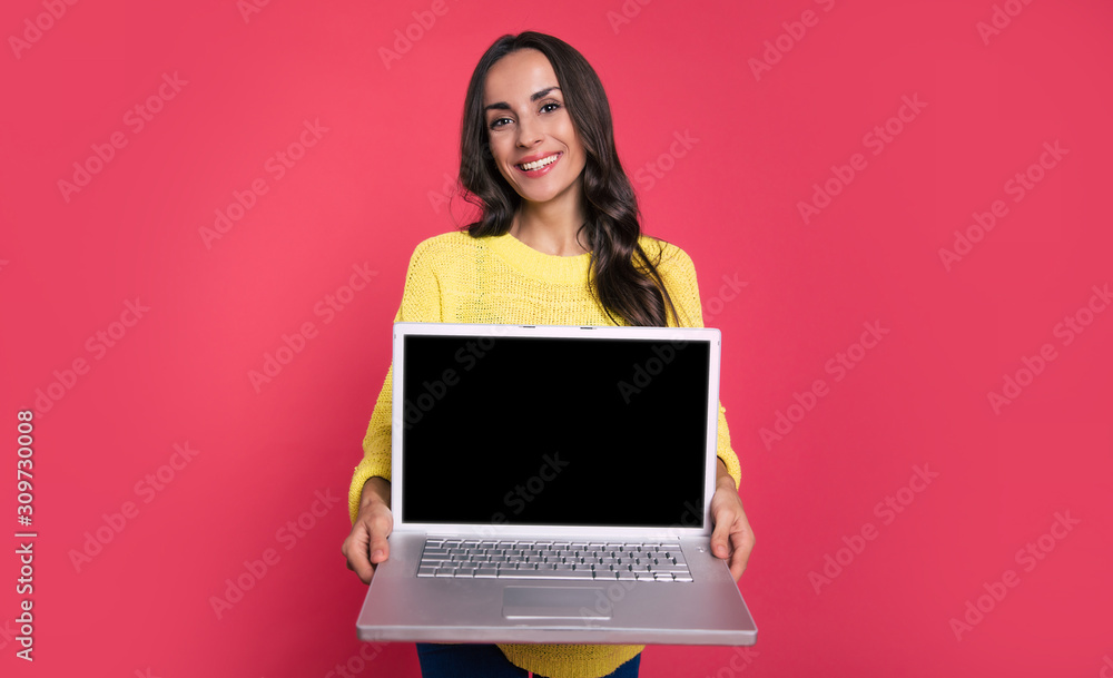 Naklejka premium Laptop review. Close-up photo of a content girl in a casual outfit, who is smiling while holding a laptop in her arms and showing it to the camera. 