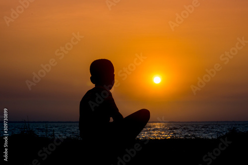 A crippled child sitting at the river watching the sunset. A day ending Sad story. photo