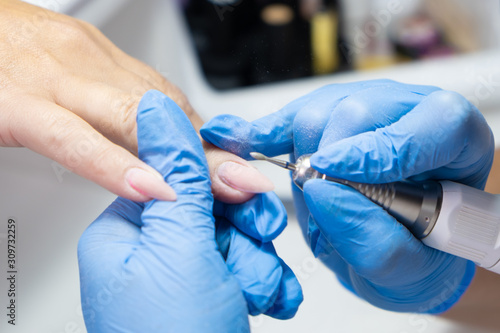 Closeup shot of hardware manicure in a beauty salon. Manicurist is applying electric nail file drill to manicure on female fingers