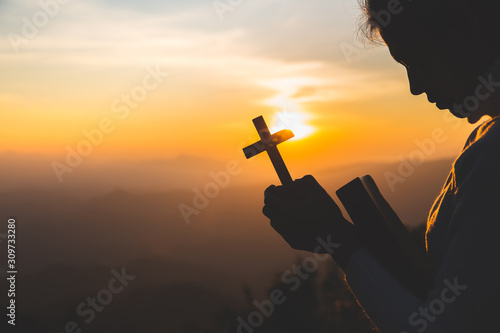 Women pray to God with the Bible and the cross  with morning sunrise. Woman Pray for god blessing to wishing have a better life. Christian life crisis prayer to god. photo