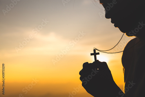 Silhouette of christian young woman praying with a cross at sunrise, Christian Religion concept background.