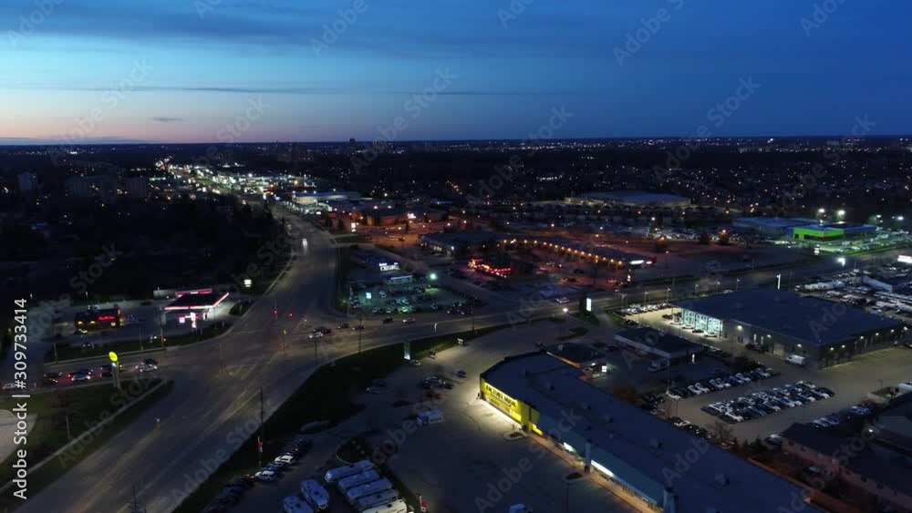 Right To Left Pan Aerial Flying Towards City Center At Night With Traffic At Intersection With Winnebegos And Trailers For Sale At Dealership Right To Left Pan Aerial Flying Towards City Center At Night With Traffic At Intersection With Winnebegos And Trailers For Sale At Dealership