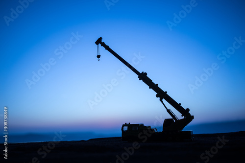 Abstract Industrial background with construction crane silhouette over amazing sunset sky. Tower crane against the evening sky. Industrial skyline. Selective focus photo