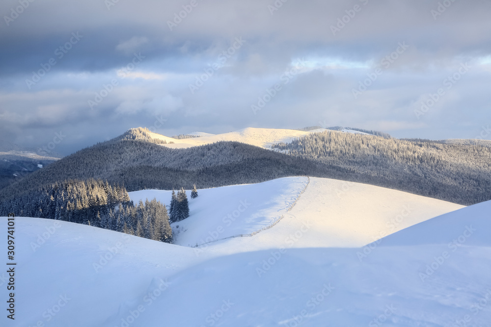 Obraz premium Winter scenery. Wooden fence. Beautiful landscape of high mountains, forest and sky with clouds. Lawn covered with white snow. Wallpaper snowy background. Location place Carpathian, Ukraine, Europe.
