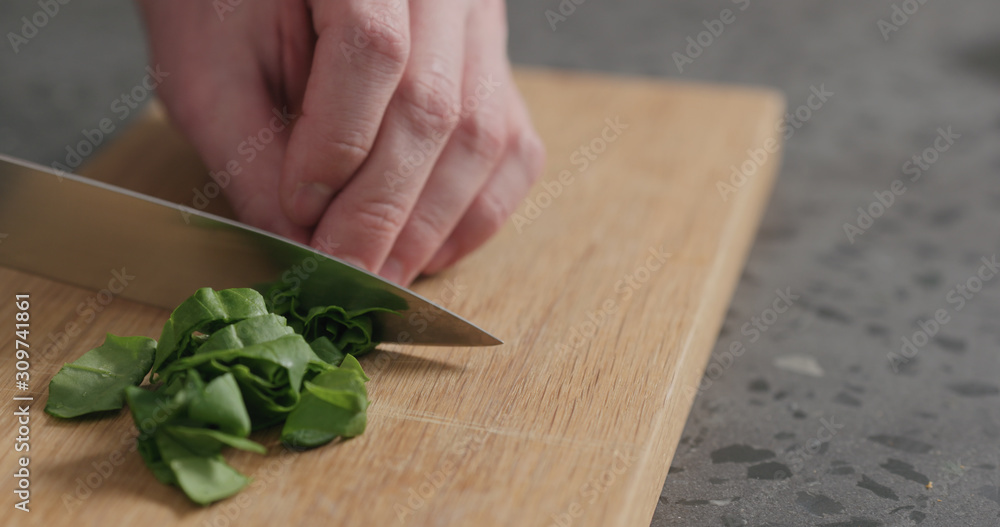 man chopping fresh spinach leaves on oak cutting board man chopping fresh spinach leaves on oak cutting board